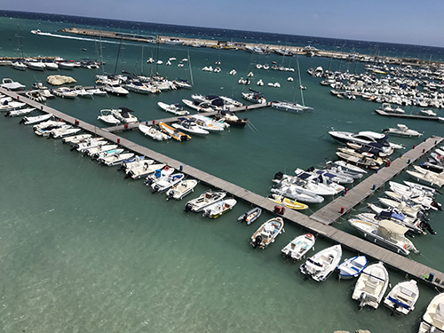 Countless boats lined up at an Italian marina against a turquoise sea