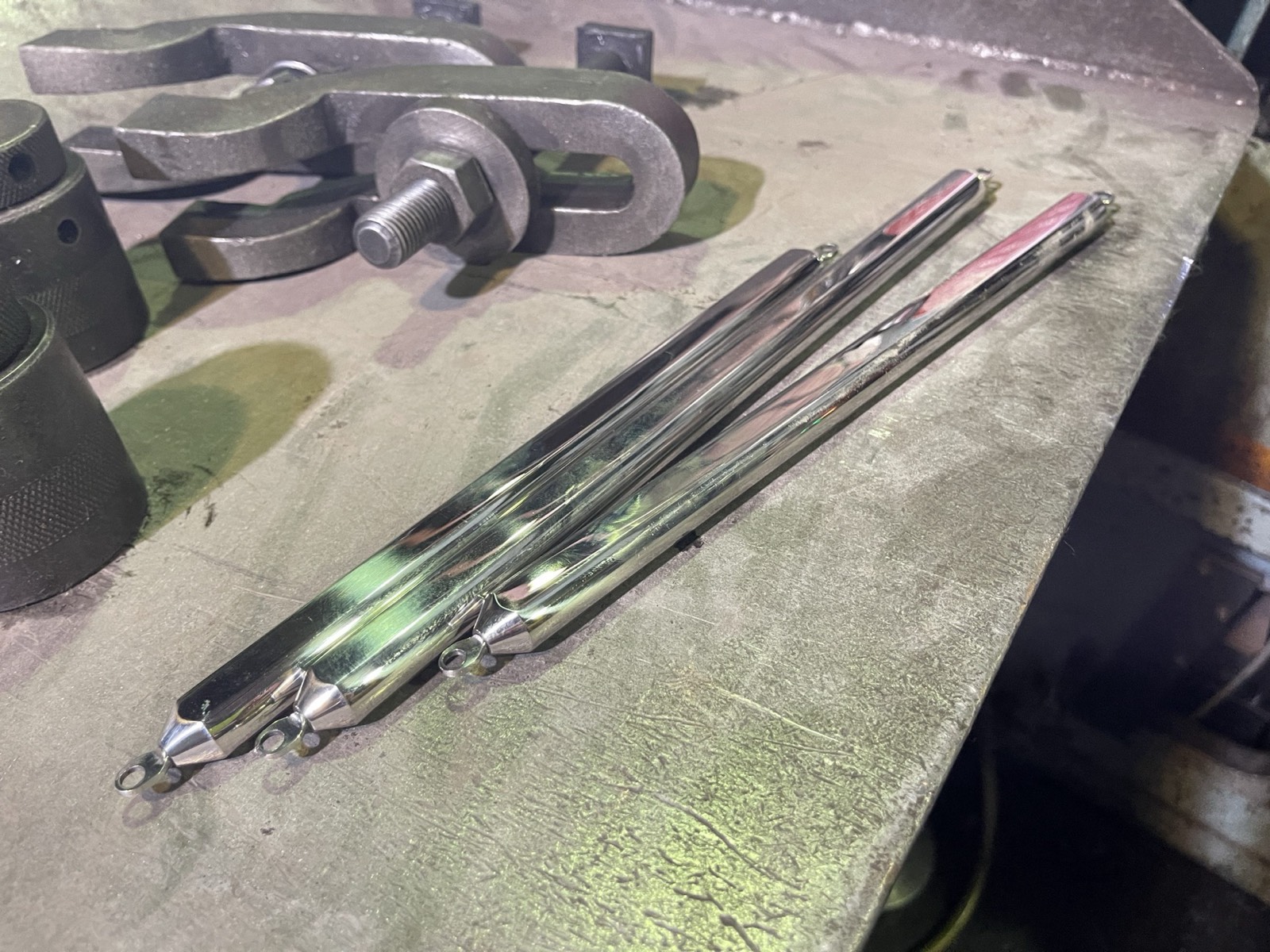 A detail of three mirror-finished ISAJIG jigs laid out on a workshop bench